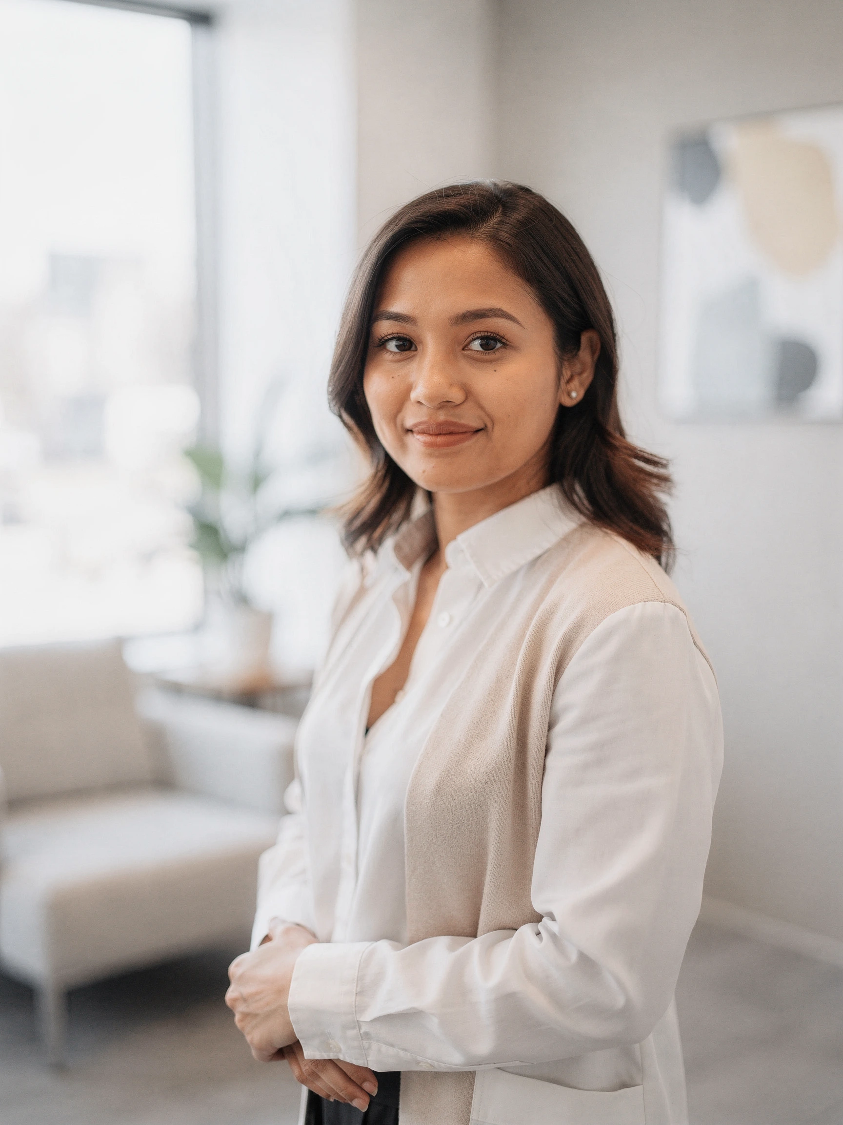 Woman in white cardigan standing in a modern clinical office with natural light and plants